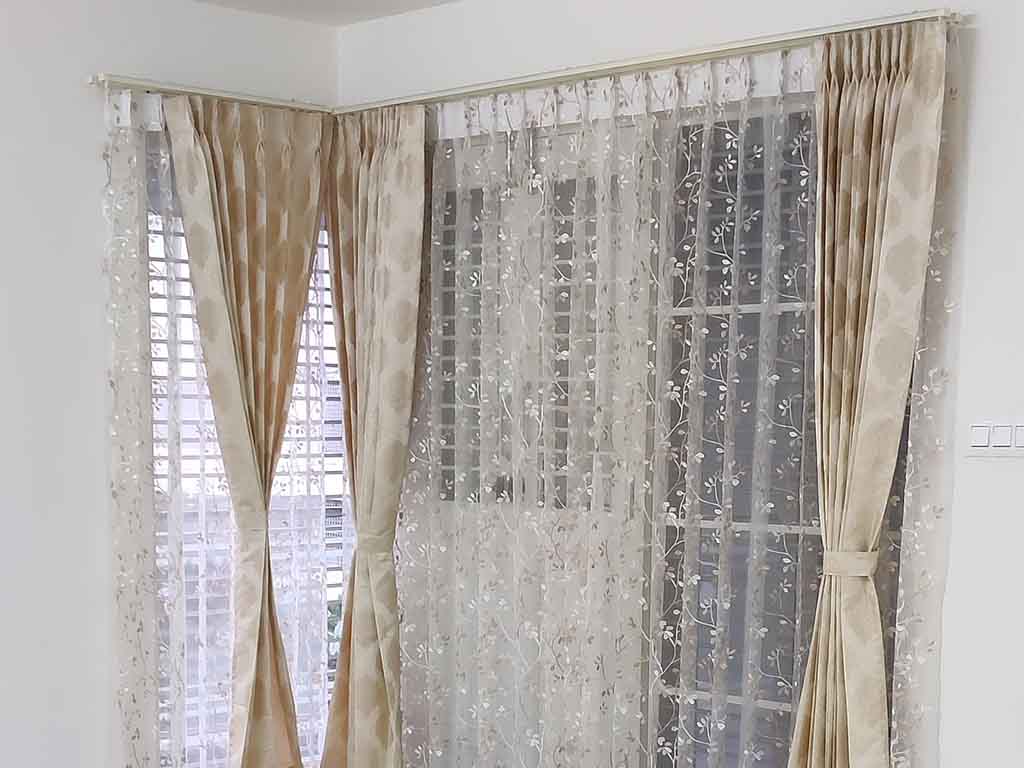 Embroidered sheers with beige drapes across a corner window